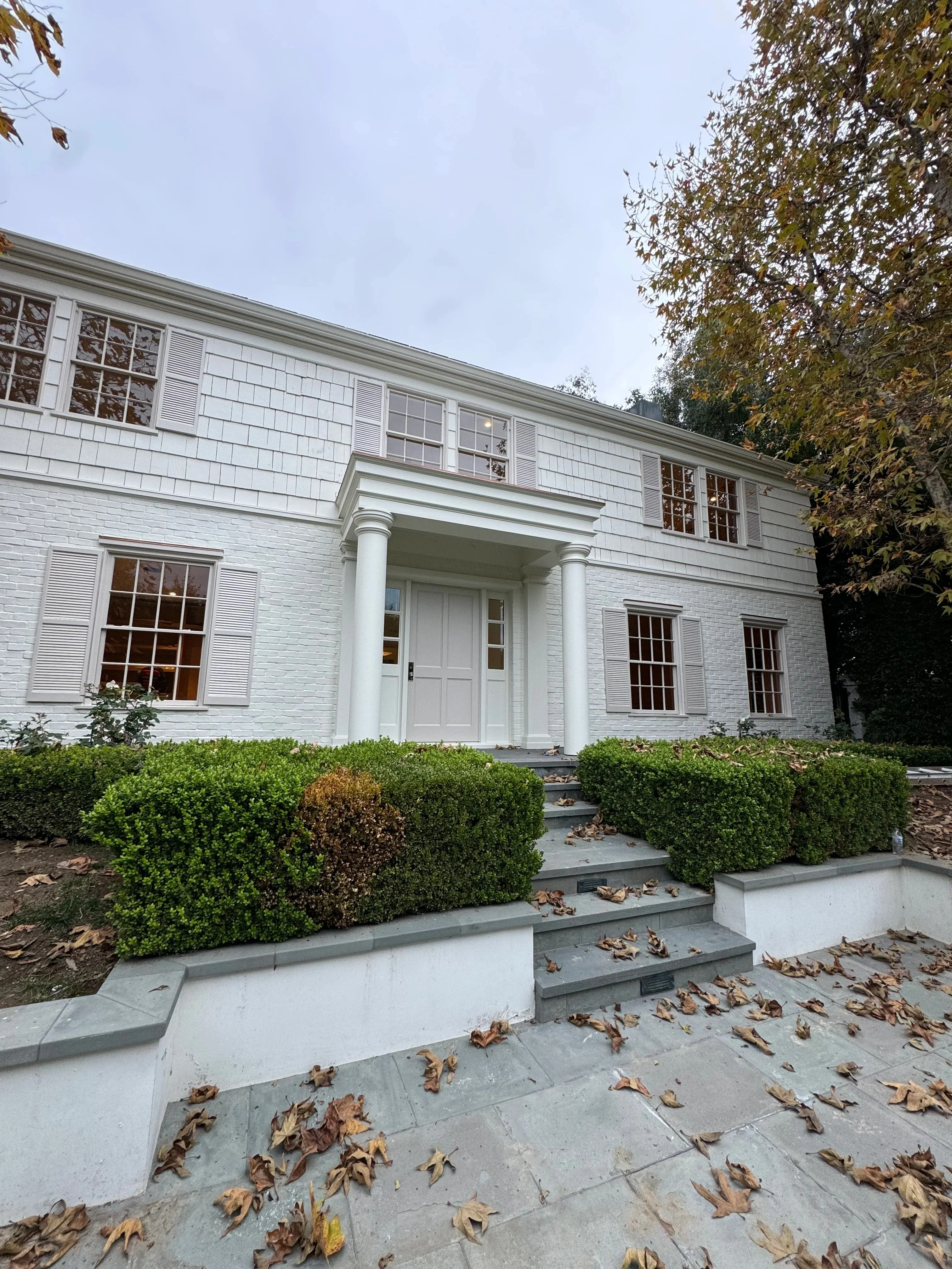 White painted colonial home with trim, columns, and shutters; stone entry steps and boxwood landscaping