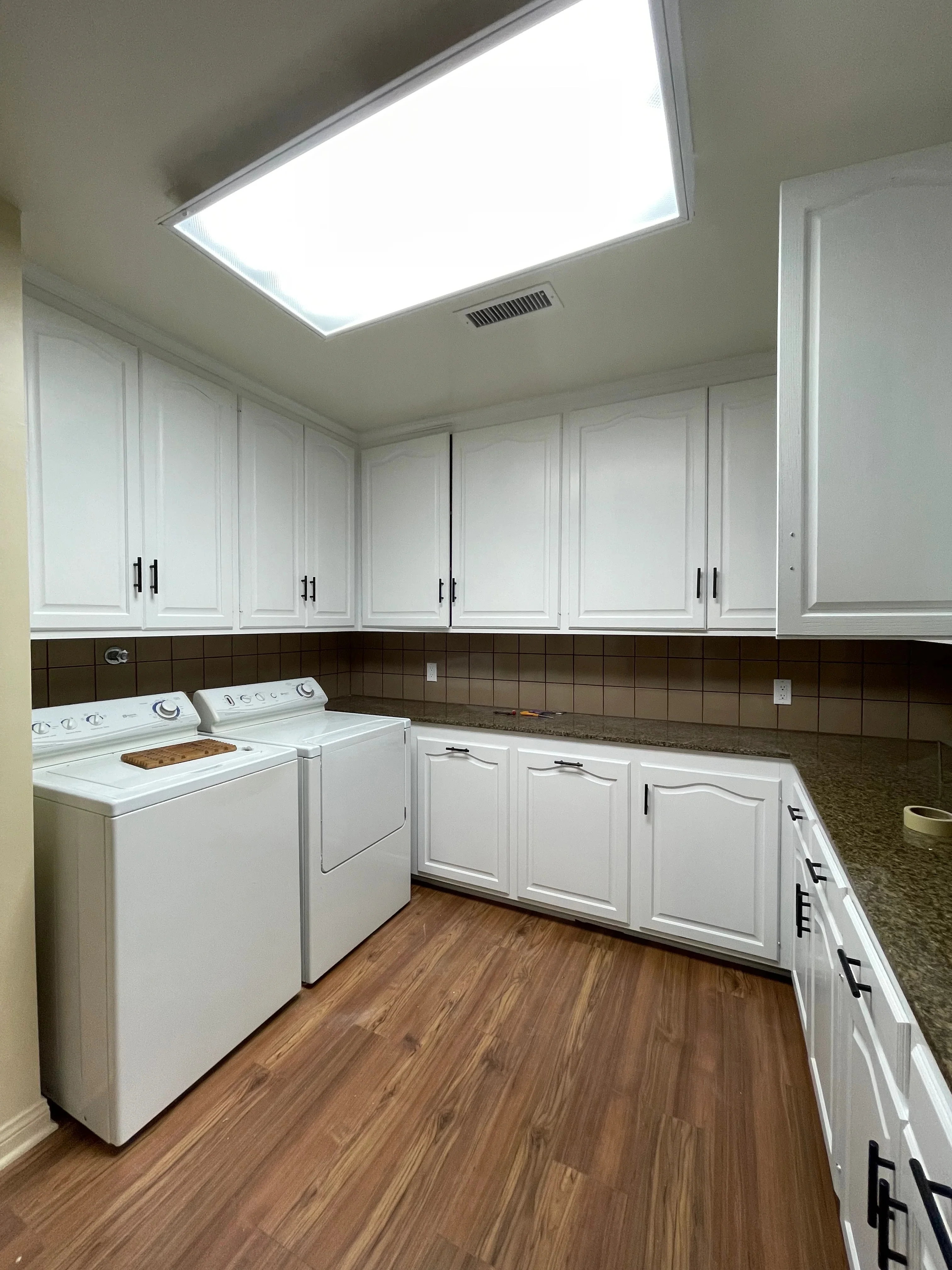 White painted laundry room cabinets with black hardware, painted trim, and recessed ceiling light