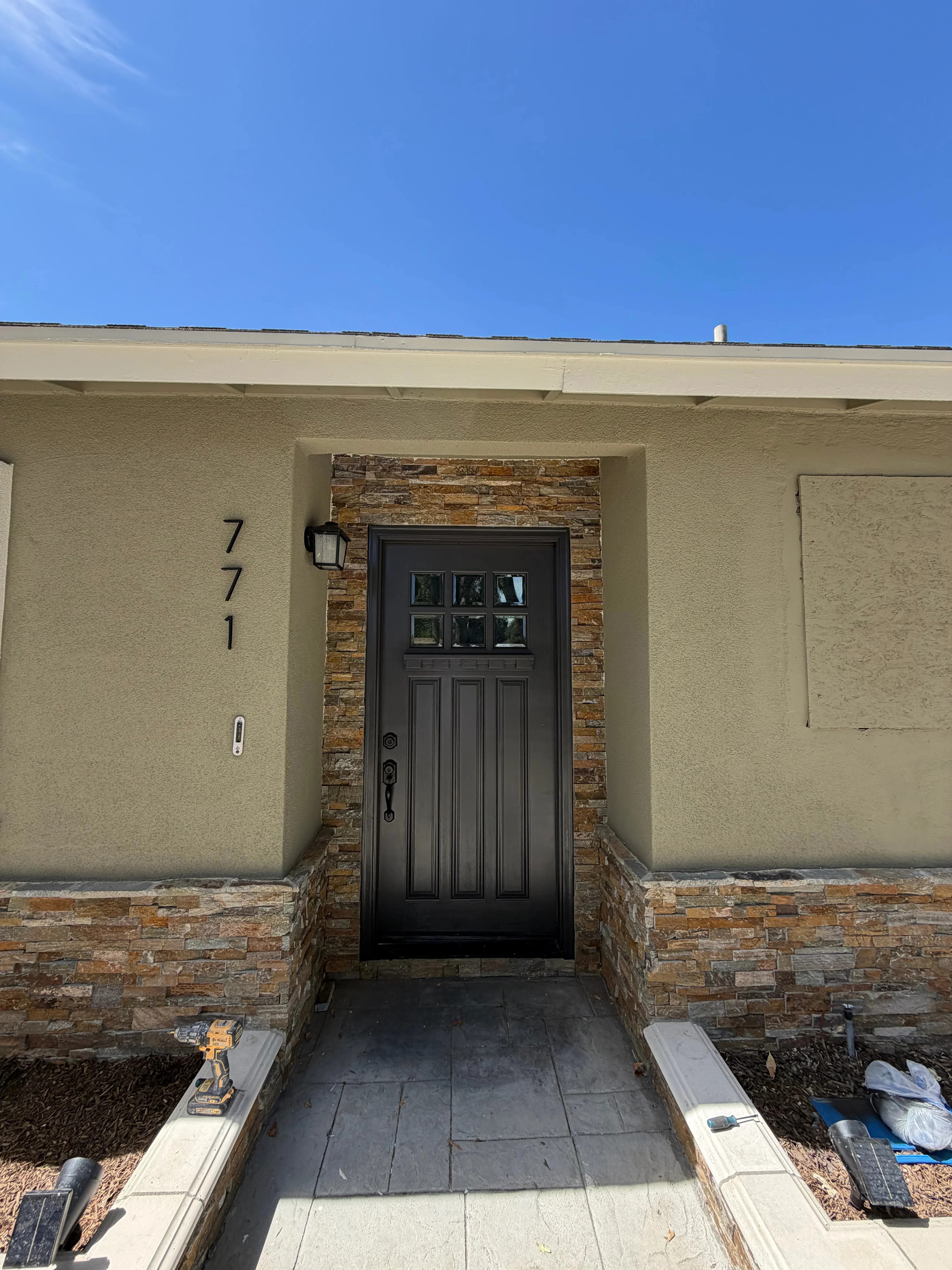 Cream stucco walls with warm-toned stone veneer entry surround and black six-panel door