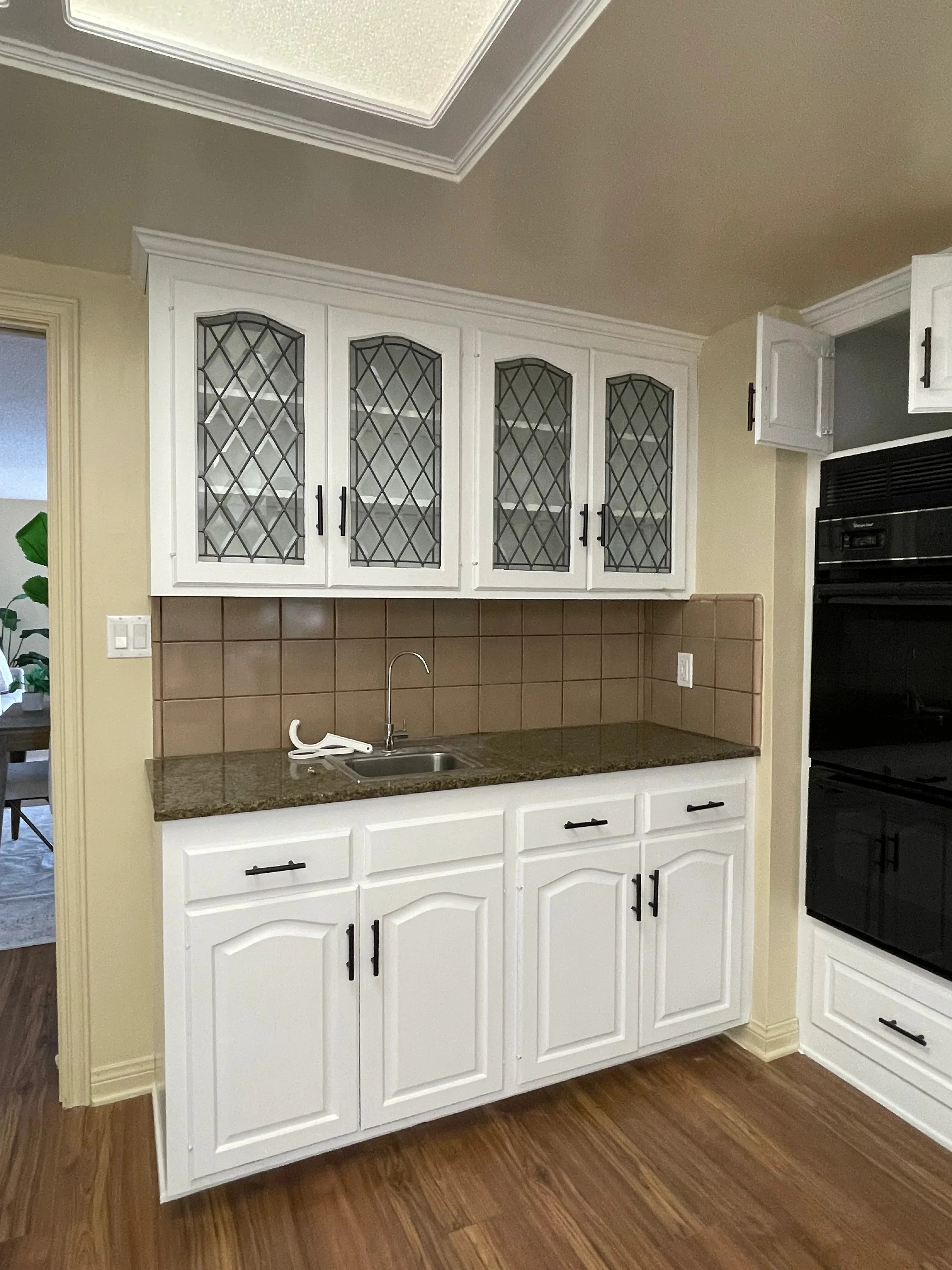 White painted kitchen cabinets with glass doors, tan tile backsplash, granite countertop, and black hardware