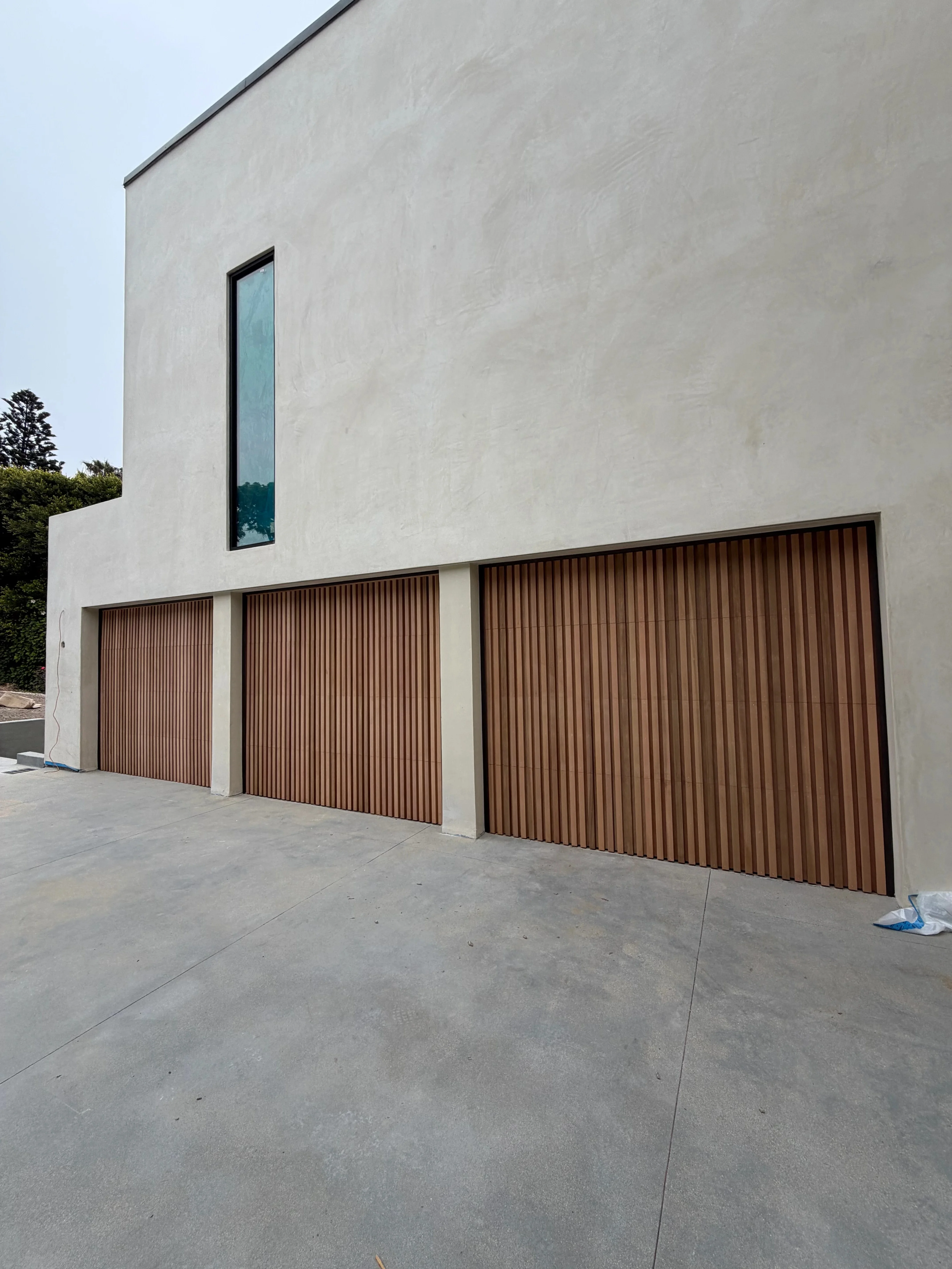 Light gray stucco exterior with brown corrugated metal garage doors and vertical window trim