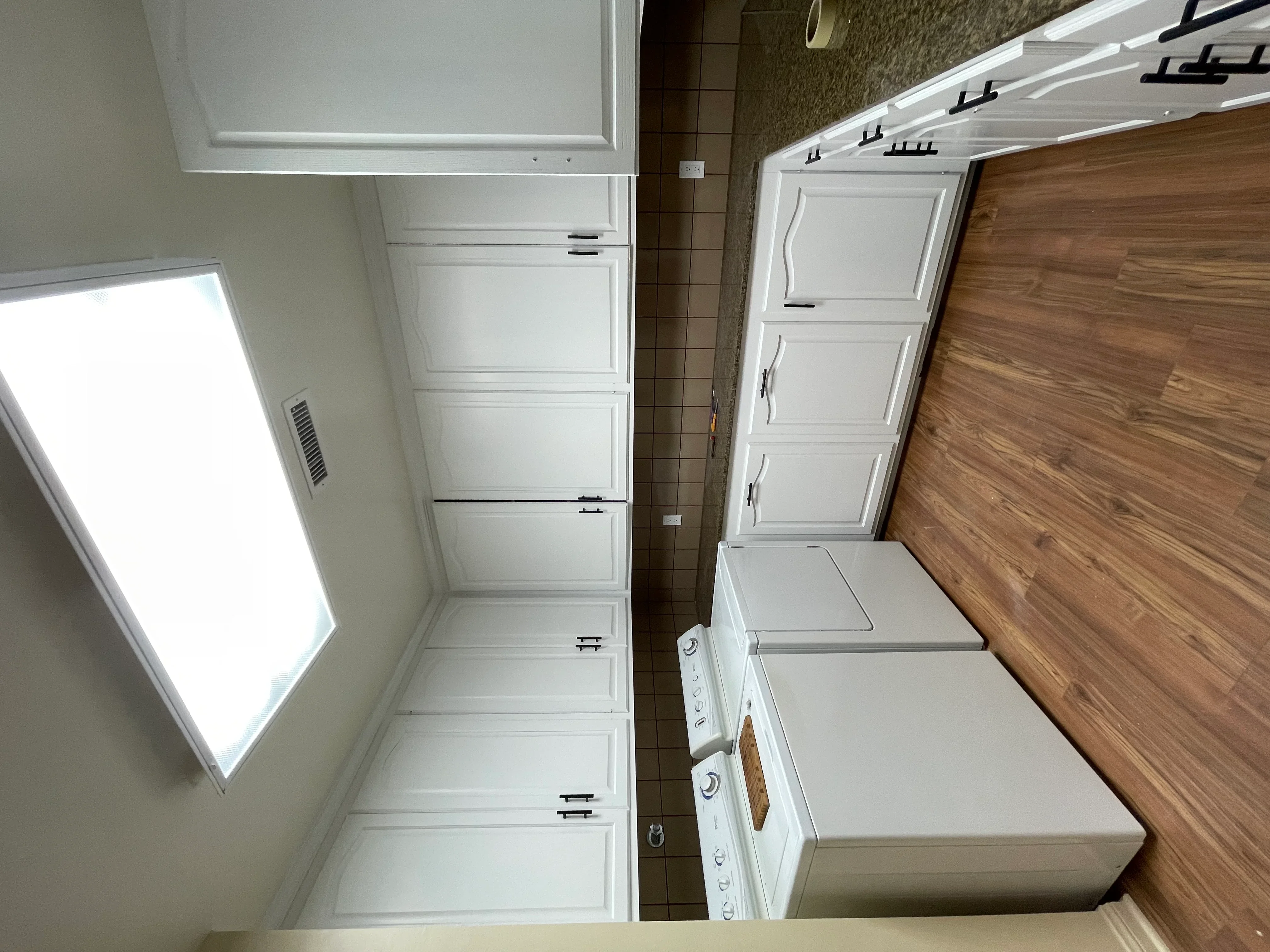 White painted laundry room cabinets, trim, and ceiling with wood flooring