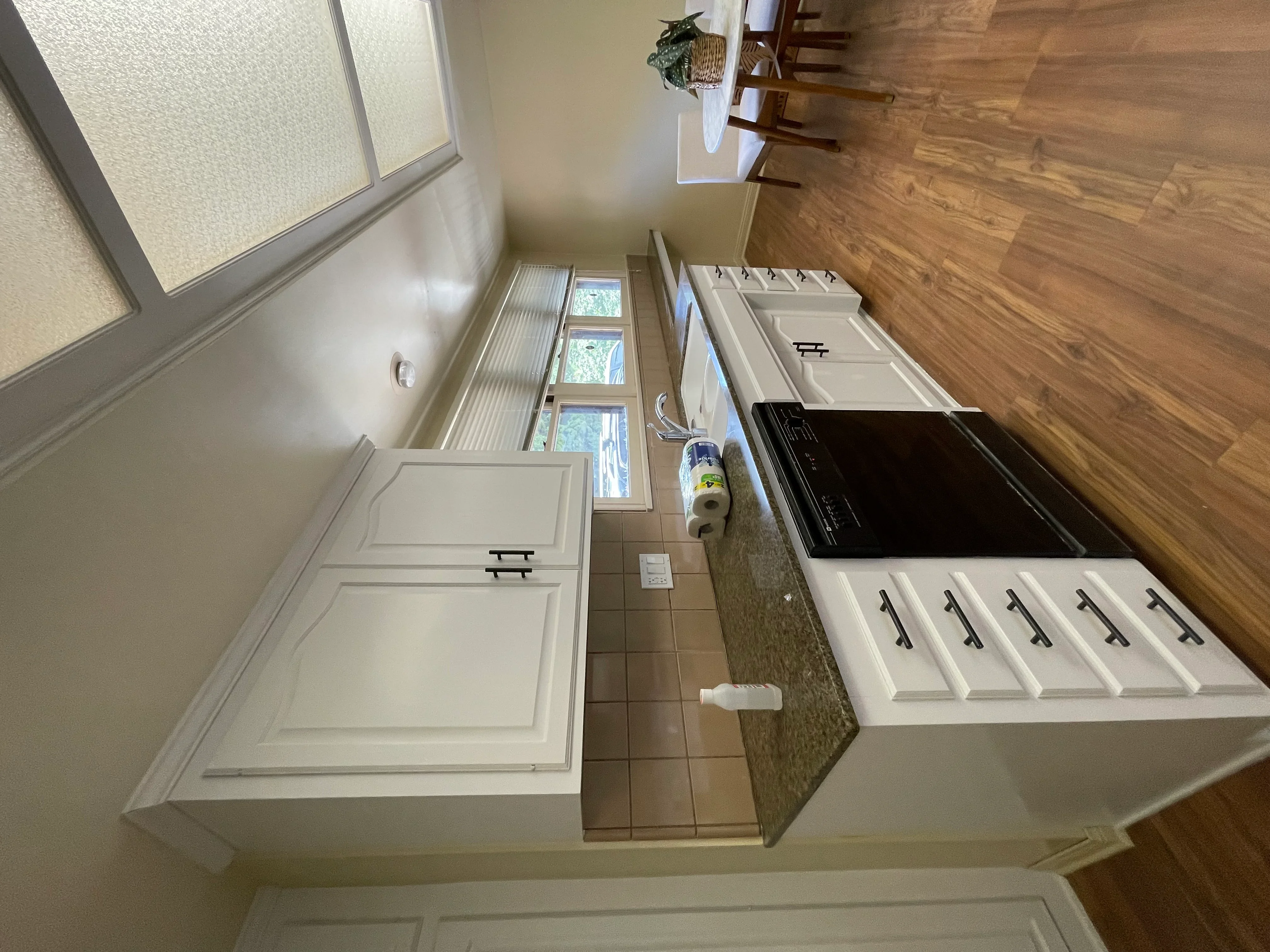 White painted kitchen cabinets with black hardware, granite countertop, and stainless steel cooktop