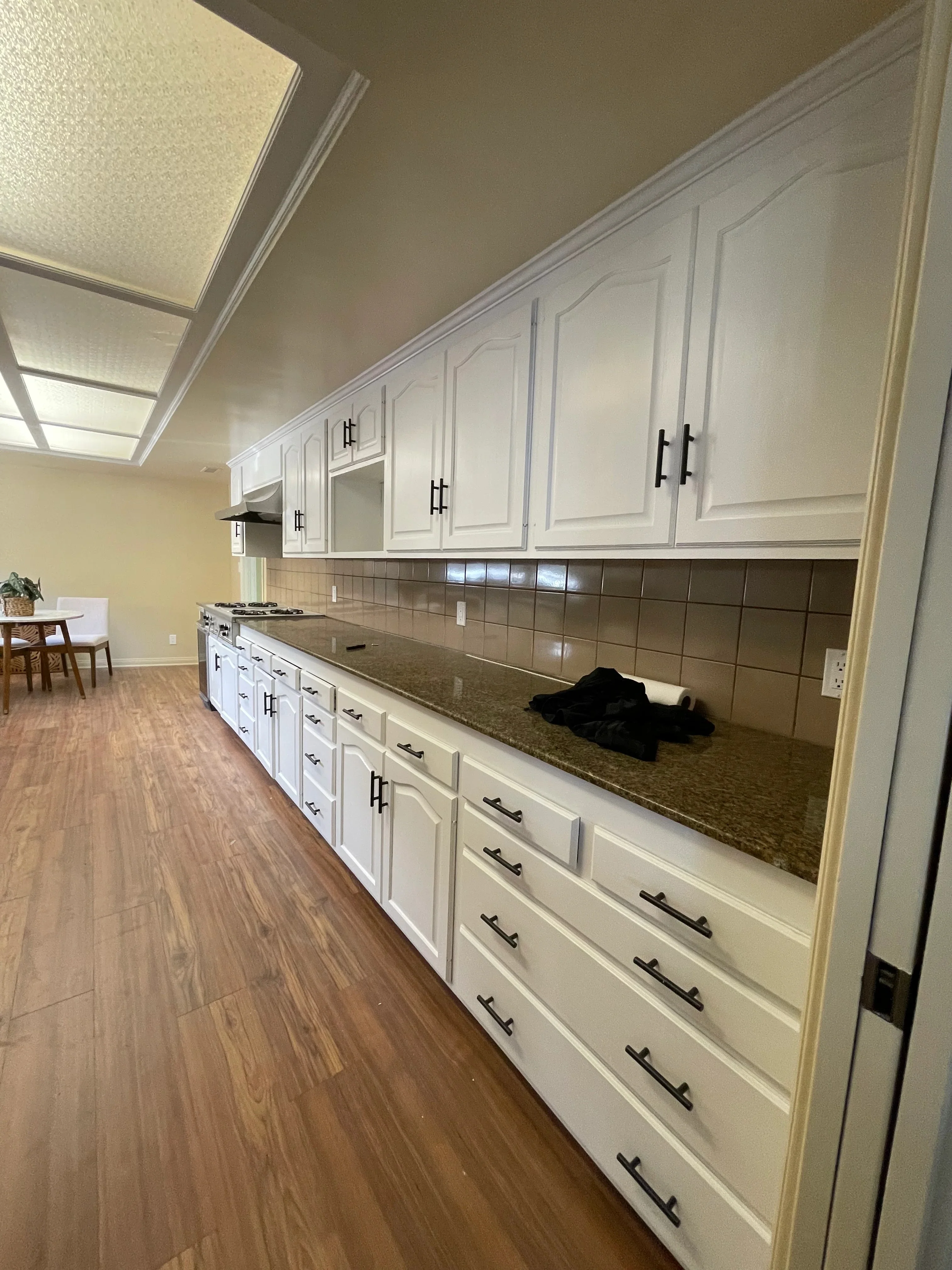 White painted kitchen cabinets with black handles, dark tile backsplash, granite countertop