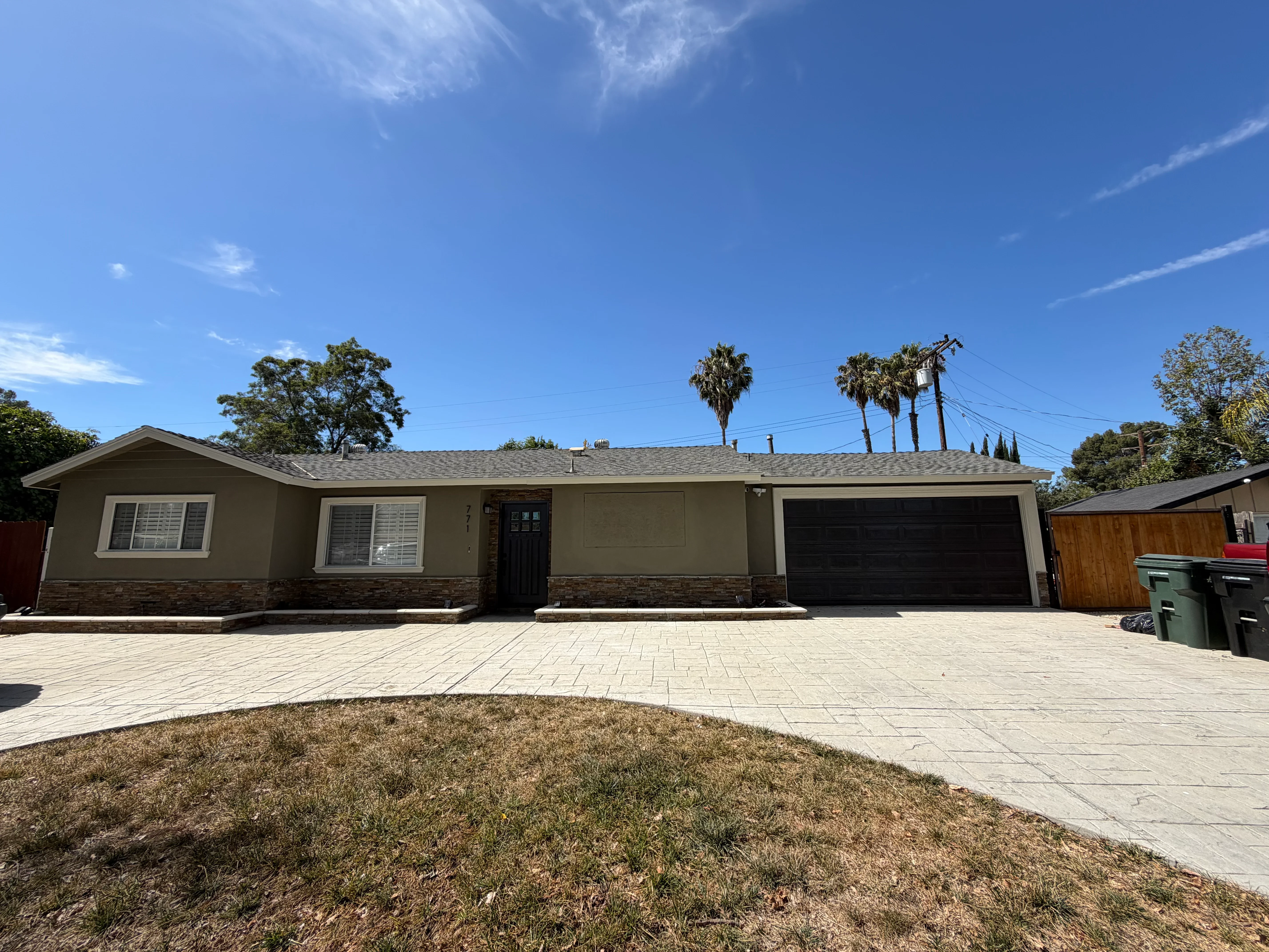 Single-story home with freshly painted taupe stucco exterior, stone veneer base, and black garage door
