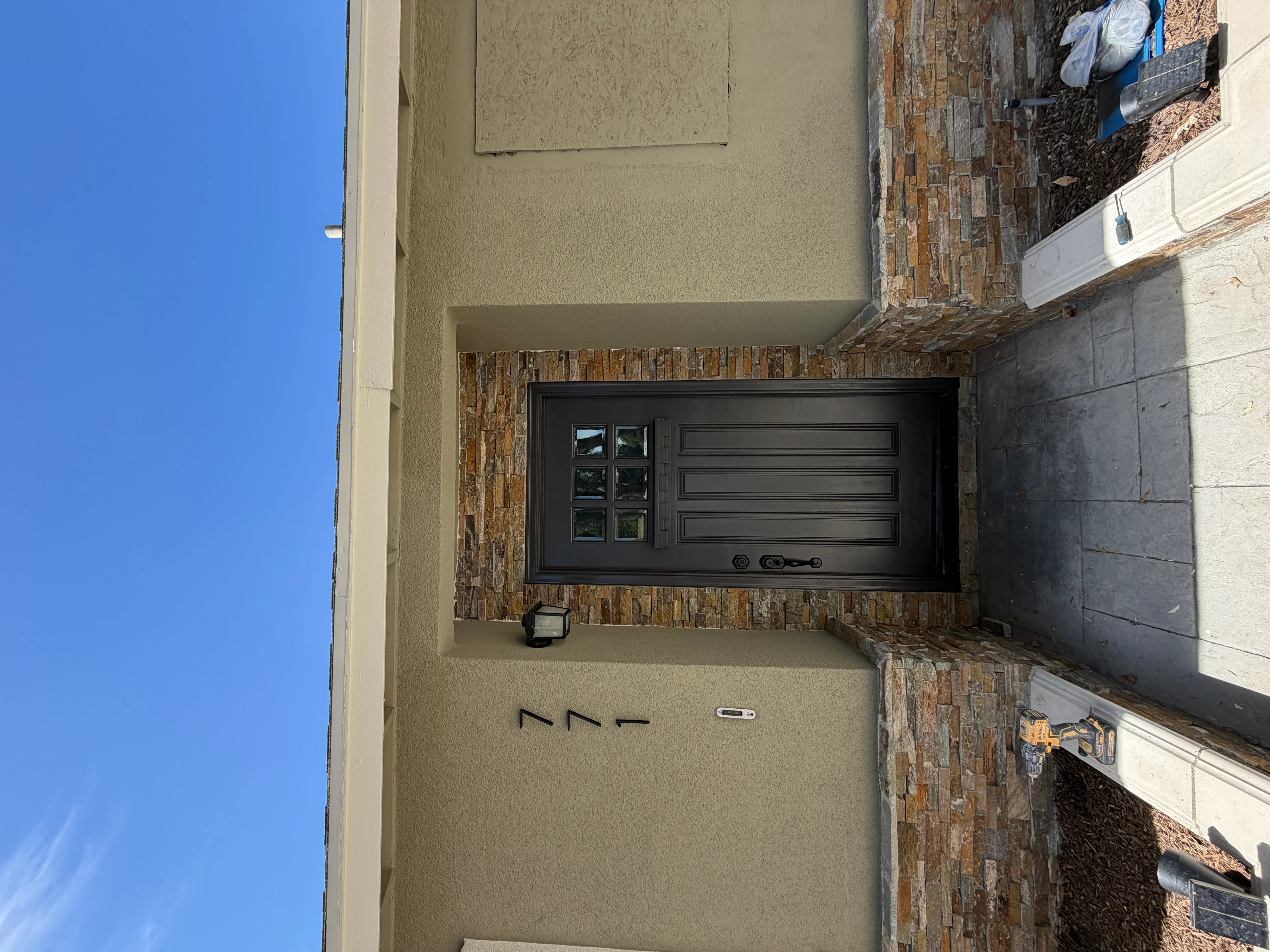 Black modern garage door with six panels and hardware on stucco wall with brick trim