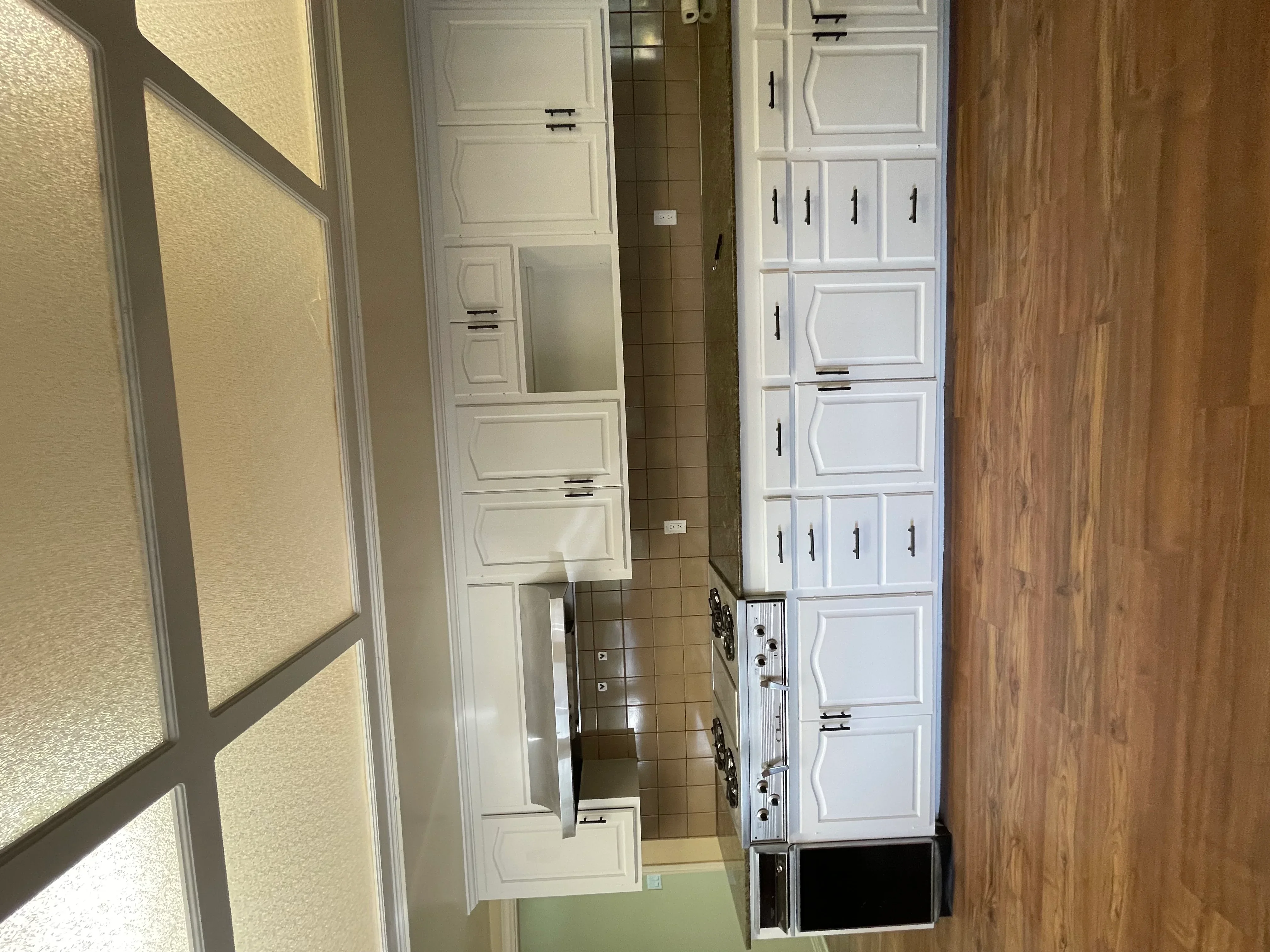 White painted kitchen cabinets with black hardware handles and raised panel doors in galley kitchen